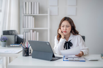 A woman is sitting at a desk with a laptop and a piece of paper