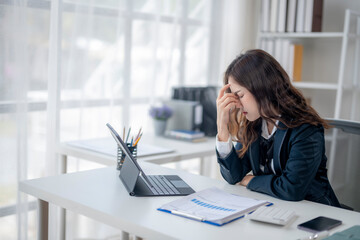 A woman is sitting at a desk with a laptop and a tablet