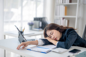 A woman is sleeping on her desk with a laptop and a stack of papers
