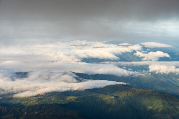 the clouds are floating over some mountains near a town and a forest