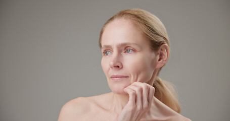 Anti age, Beauty, health and dry skin care concept - beautiful middle-aged mature Caucasian woman in her 50s touching her face skin and looking at the camera with a slight smile