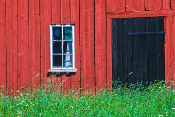 Old barn with a door and a window and high grass and wildflowers