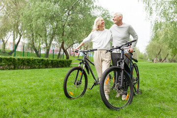 elderly senior couple rides bicycle in the park in the summer and smiles, old gray-haired man and...