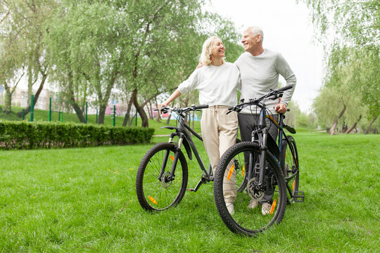 elderly senior couple rides bicycle in the park in the summer and smiles, old gray-haired man and woman are actively resting outdoors, old people practice cycling in forest - Powered by Adobe