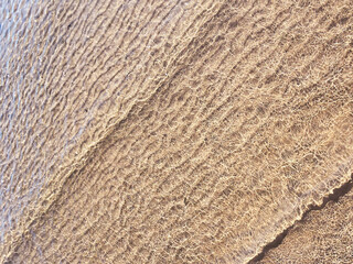 Small waves gently lap the sandy shore in this golden, textured beach pattern.