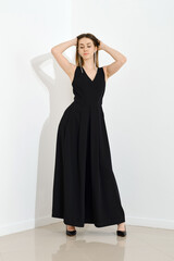 Fototapeta premium Stylish young woman in a long black dress with a low neckline threw her arms behind her head