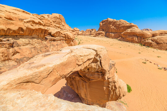 Tranquil scene atop the famous Um Fruth rock arch in the vast Wadi Rum desert, Jordan, admiring the expansive sandy landscape under a clear blue sky