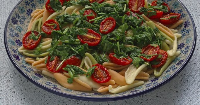Tricolore  Foglie d'Ulivo pasta in the shape of olive leaves with wilted rucola and tomatoes. Italian cuisine. Table spin.