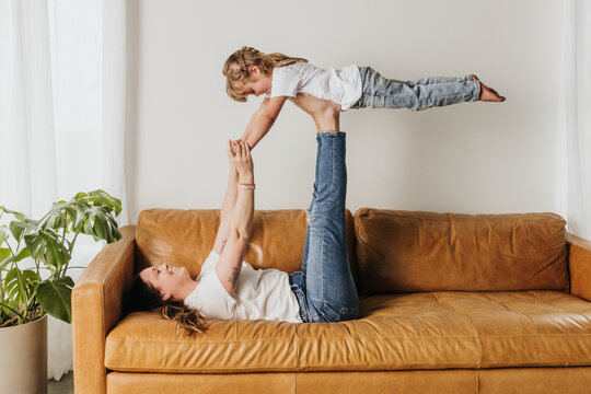 mom lays on couch while holding daughter up with her feet