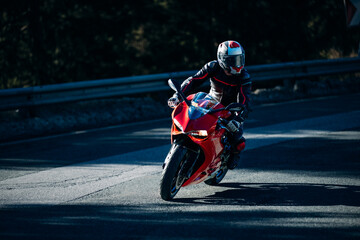 Motorcyclist leans on red racing bike in curve shadow and sunlight