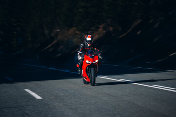 Motorcyclist leans on red racing bike between shadow and sunlight