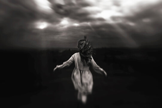 Back view of young girl hair blowing walking towards stormy sky
