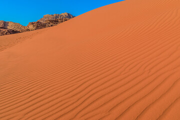 Serene sunset view capturing the textured sands of Wadi Rum, Jordan, with the gentle contours of the landscape leading towards distant mountains under a clear, brightening sky