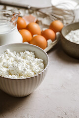 Cottage cheese in a ceramic bowl, jug of milk, flour and eggs. Ingredients for cooking