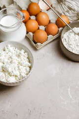 Cottage cheese in a ceramic bowl, jug of milk, flour and eggs. Ingredients for cooking. Copy space for text