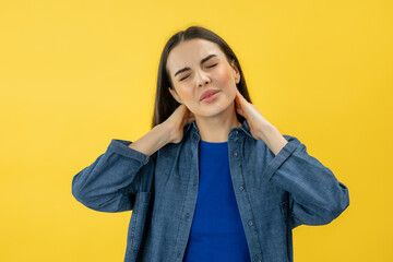 tired upset woman standing massaging neck to relieve pain, muscle strain in back isolated on yellow background.