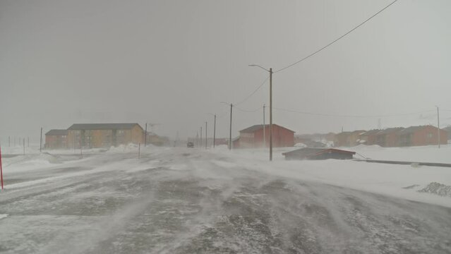 A car vanishes into the distance while the wind moves snow accross an empty road in Longyearbyen, Svalbard.