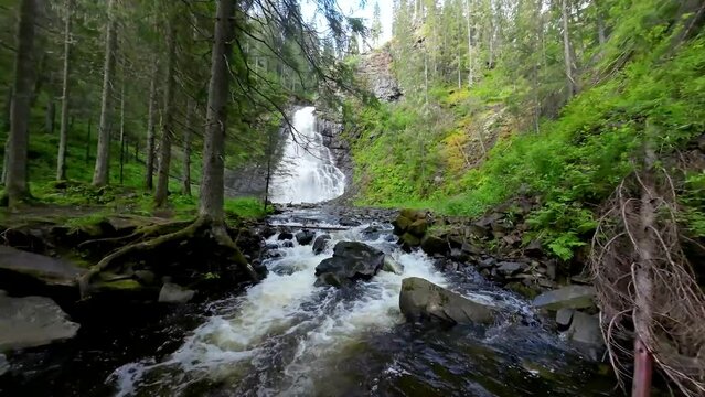 A scenic view of Flokofallet waterfall in Norway, surrounded by lush green forest and a rushing stream.
