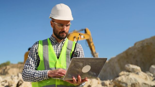 Civil engineer working in quarry use a laptop to check the operation of the yellow excavator