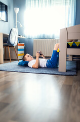 Boy playing video game on smartphone laying on floor in his room.
