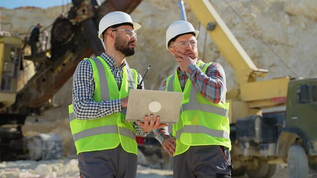 Construction workers engineers in uniform with laptop are talking at the quarry mining site
