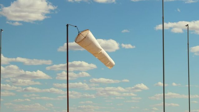 A white windsock blows in the breeze on a sunny day. Useful for concepts about weather, wind, direction, or travel.