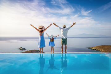A happy family on summer holidays stands by the swimming pool and enjoys the beautiful view behind the mediterranean sea in Greece