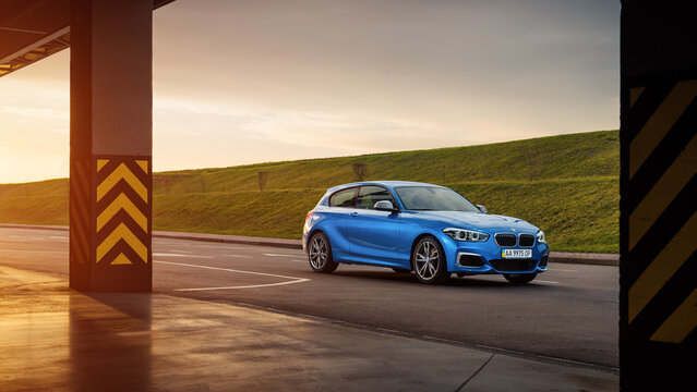 Blue BMW 1-series (F21) on a parking lot at sunset. Three quarter front view of sporty BMW M140i hatchback with two pillars in the foreground closer to the to camera. Kyiv, Ukraine - April 03, 2016: 