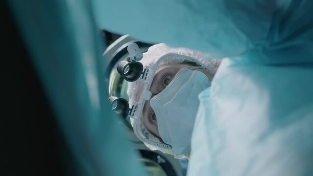 Bottom view shot of focused Caucasian adult female doctor wearing magnifying glasses working at operating room