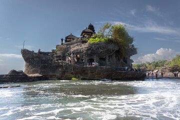 Shot of people on rock at water's edge, gripping onto waves