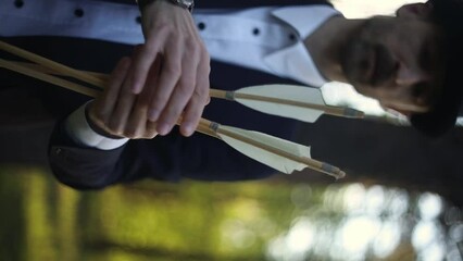 a man in a suit in the forest, holding arrows in his hands, close-up of hands with arrows. three arrows in male hands, close-up, surreal video. The video was shot on a Soviet lens, soft focus.
