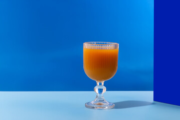 A glass of refreshing orange juice with a blue tint is placed on a table