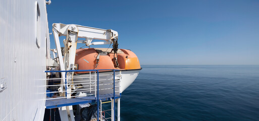 Lifeboat next to a ferry boat on a summer day with calm blue seas. Wide image