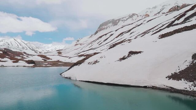 Suraj Tal lake with turquoise water and snow covered mountains in Lahaul, Himachal Pradesh, India. Blue calm lake surrounded by snow capped mountains in Indian Himalayas. Reflection of sky in lake
