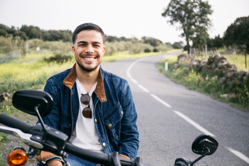 Smiling young biker sitting on motorcycle in countryside