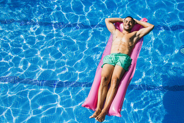 Shirtless handsome young man with hands behind head relaxing on airbed in swimming pool