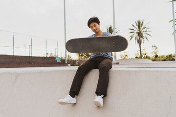 Young Chinese man sitting on wall of a skate park near the beach