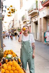 Portrait of laughing young woman on shopping street covering eye with an orange