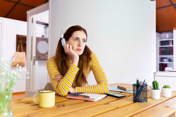 Thoughtful young woman wearing headphones while sitting at desk
