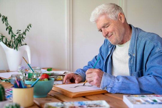 Happy senior man painting on paper at table