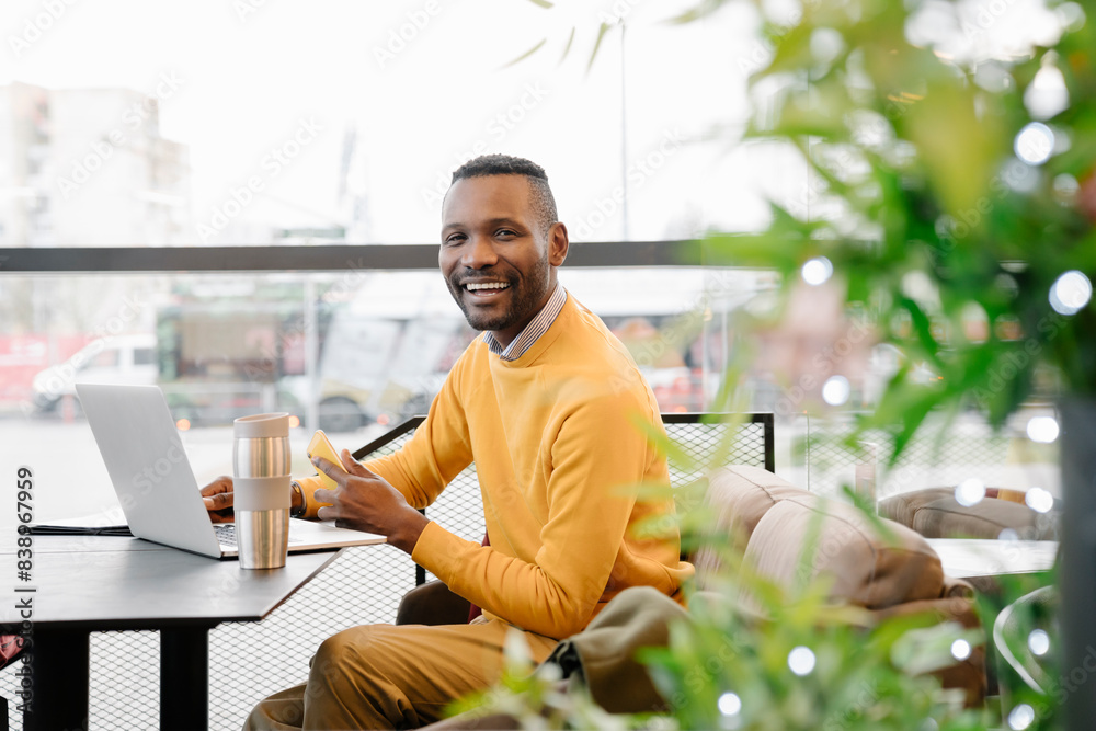 Poster Portrait of a happy man with smartphone and laptop in a cafe