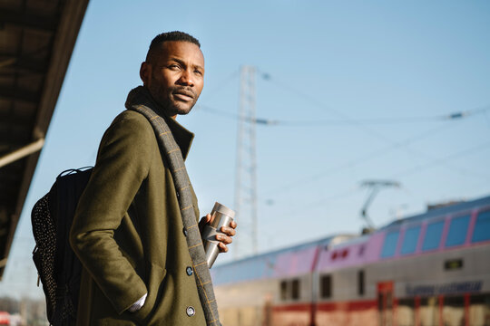 Stylish man with reusable cup waiting for the train