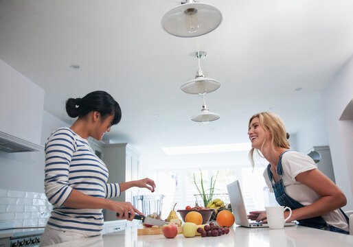 Two friends preparing fresh smoothie, chopping fruits in the kitchen