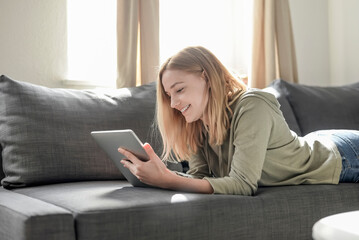 Portrait of smiling young woman lying on the couch at home using digital tablet