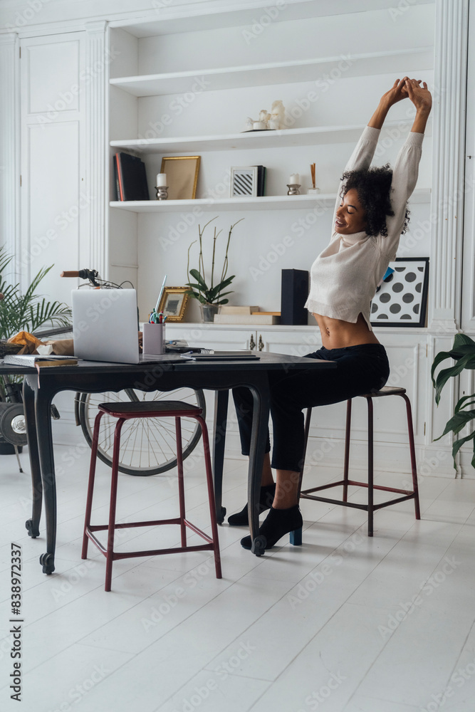 Poster Mid adult woman sitting in her home office, smiling and stretching