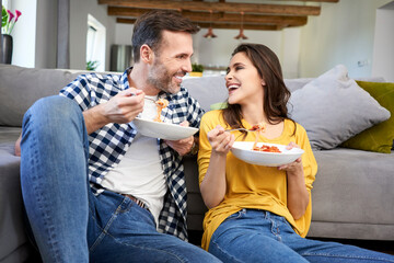 Couple sitting in living room, eating spaghetti