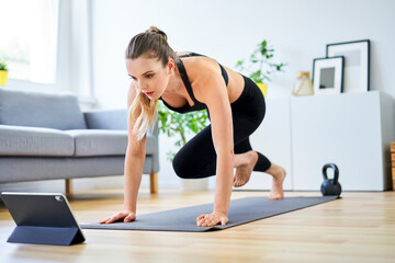 Determined woman learning mountain climber exercise through internet on digital tablet