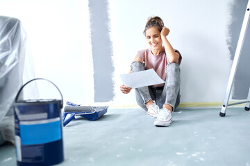 Smiling woman with head in hands holding paper while sitting on floor at home