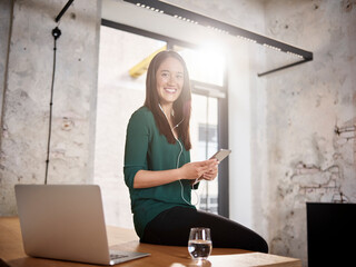 Smiling woman sitting on desk in office listening to music