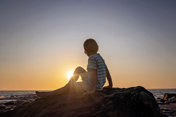 Happy children, enjoying sunset over the ocean with their family, rocky beach